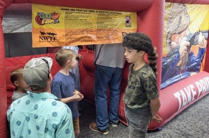 A group of children reading the ten shooting safety rules banner at the entrance to the NWTF youth range.