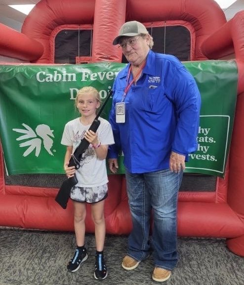 A young girl holds an air rifle beside a National Wild Turkey Federation volunteer at the WWCA youth shooting range.