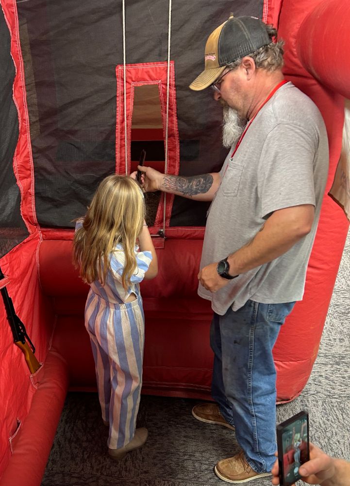 A certified volunteer instructor guides a young girl's grip and stance on the firing line of the WWCA youth range.
