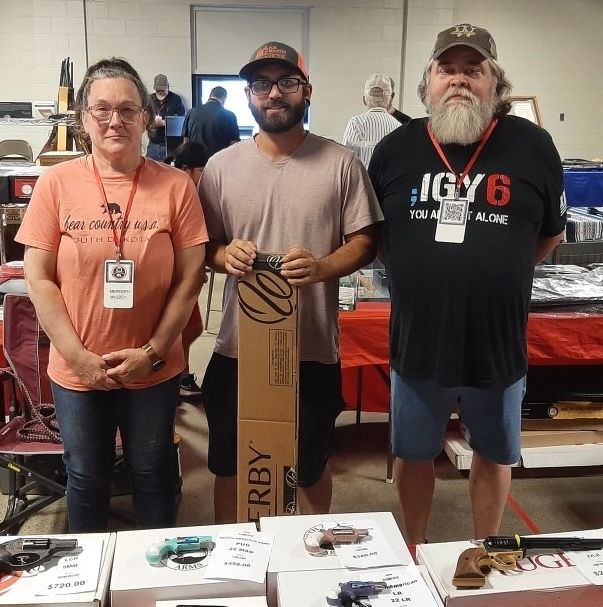 A Weatherby rifle raffle winner standing between two WWCA volunteers at the prize table.