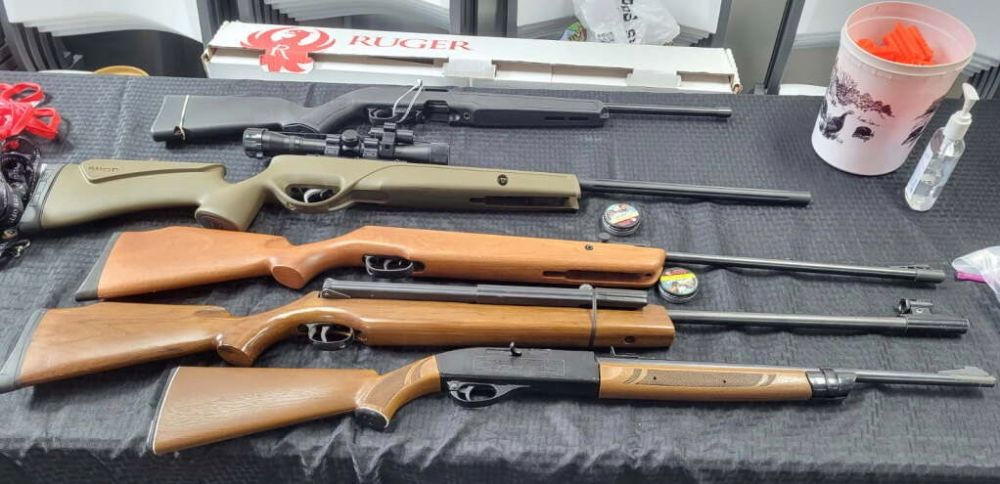Air rifles and BB guns laid out on a table with pellets and safety equipment for the youth range.